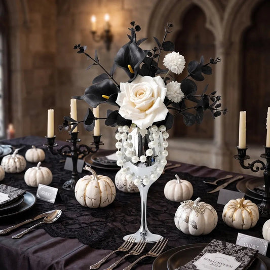 Gothic faux flower arrangement with white rose and black calla lilies in silver goblet vase styled on a dark table with white pumpkins and candles
