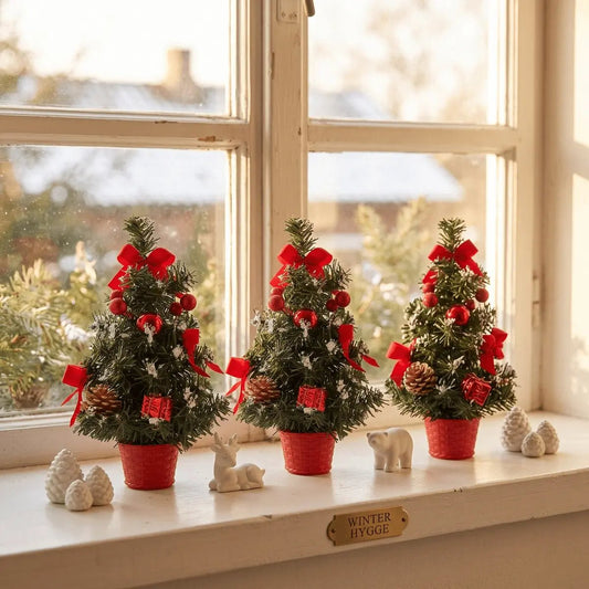 Three red artificial mini tabletop Christmas trees with ornaments displayed on a windowsill for Christmas home decoration
