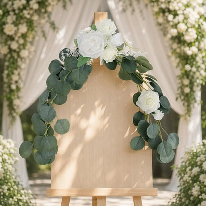 White rose silver dollar eucalyptus swag set of 2 draped diagonally on wood easel welcome sign board in outdoor garden wedding with white drape backdrop – IPOPU